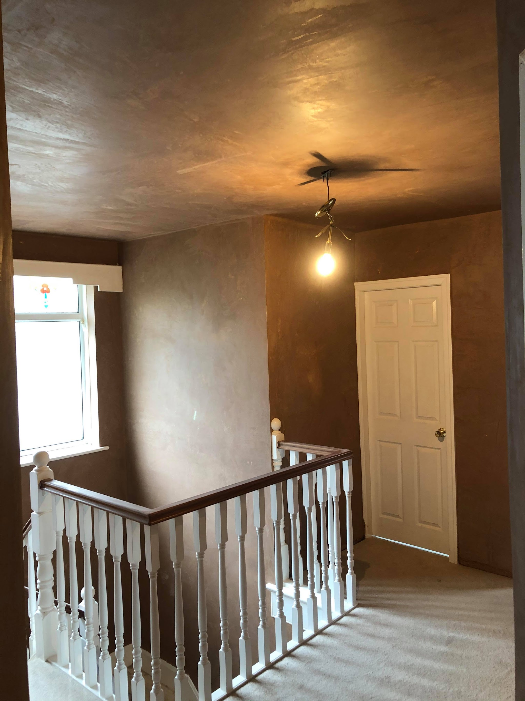 A landing and stairwell freshly plastered, with a white door and spindles